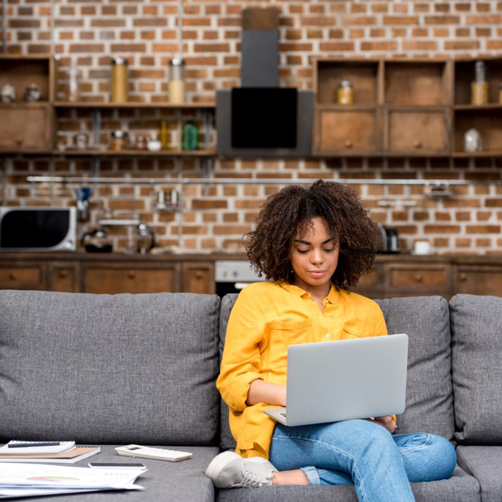 Woman working on her laptop, sat on a sofa in a living room