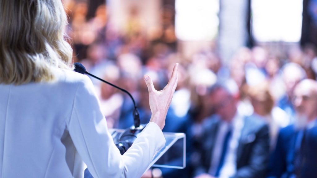 image of woman talking on podium to an audience