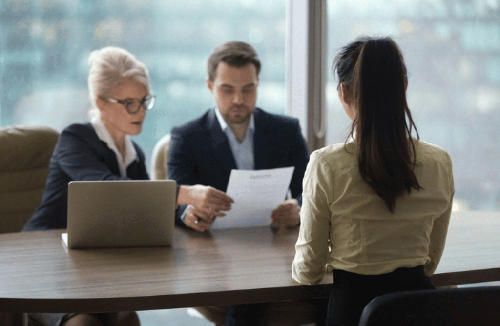 A woman converses with two hiring managers at a table, indicating a meeting taking place.